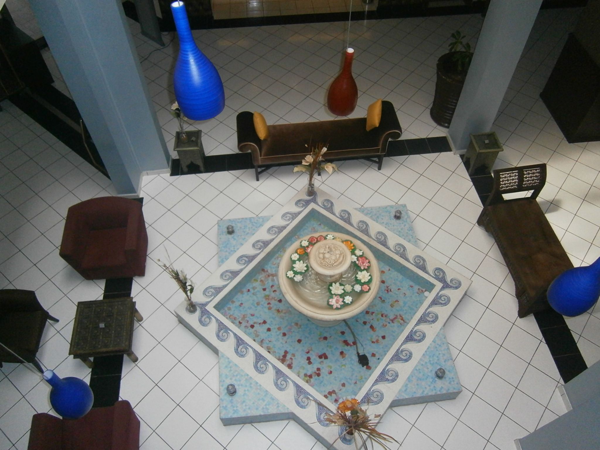 A tiled floor with a central decorative area featuring a floral arrangement, surrounded by furniture and vases.