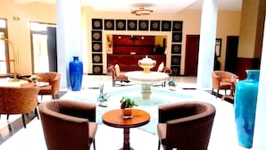 Un vestíbulo con una fuente central, áreas de descanso y una mesa de recepción.