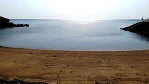 Una playa con agua tranquila, una orilla arenosa y un promontorio rocoso a la izquierda.