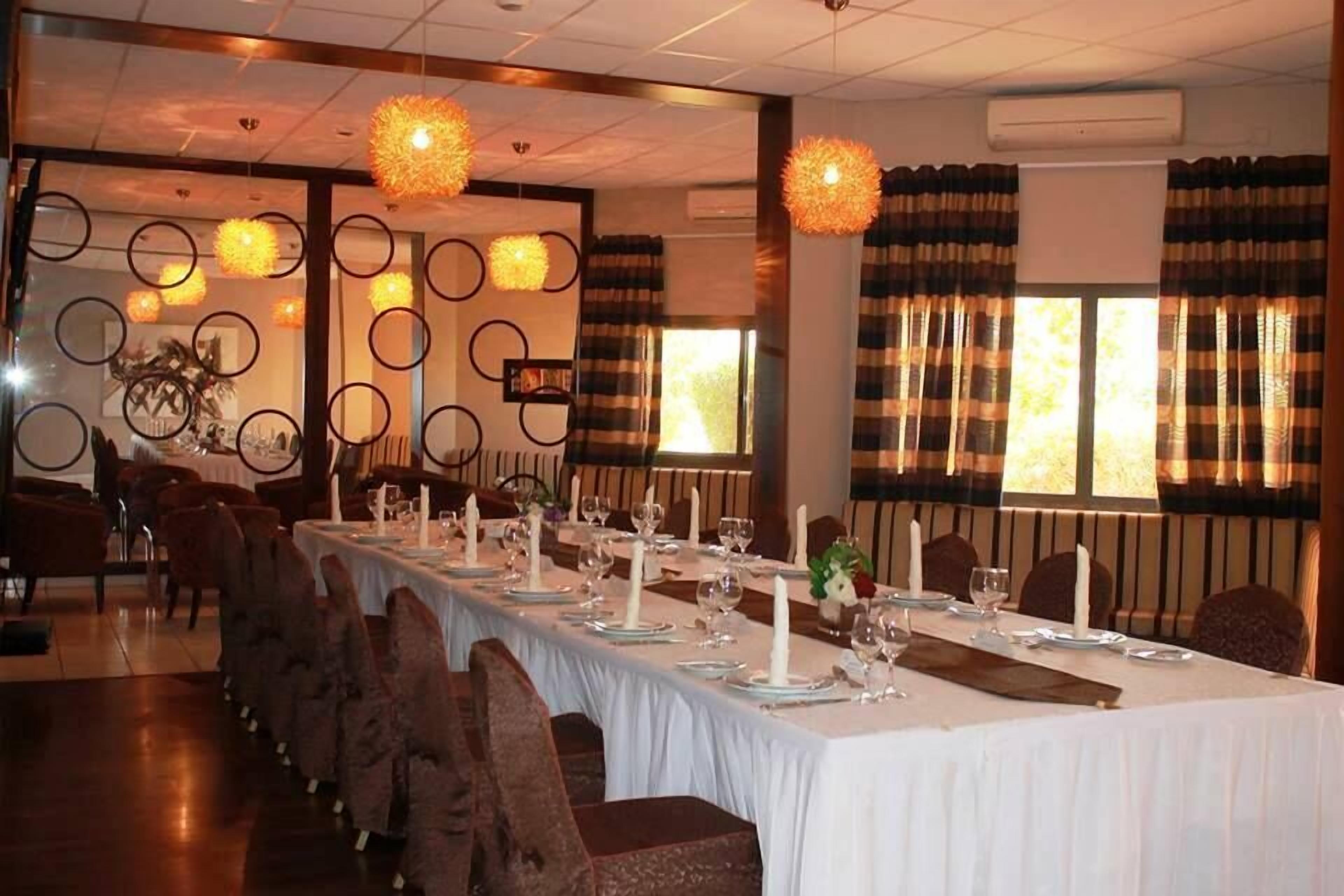 Una larga mesa de comedor cubierta con manteles blancos, velas y cristalería, con un candelabro moderno y cortinas a rayas al fondo.