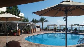 Relax by the pool surrounded by comfortable lounge chairs and umbrellas, with a pergola and lush greenery nearby.