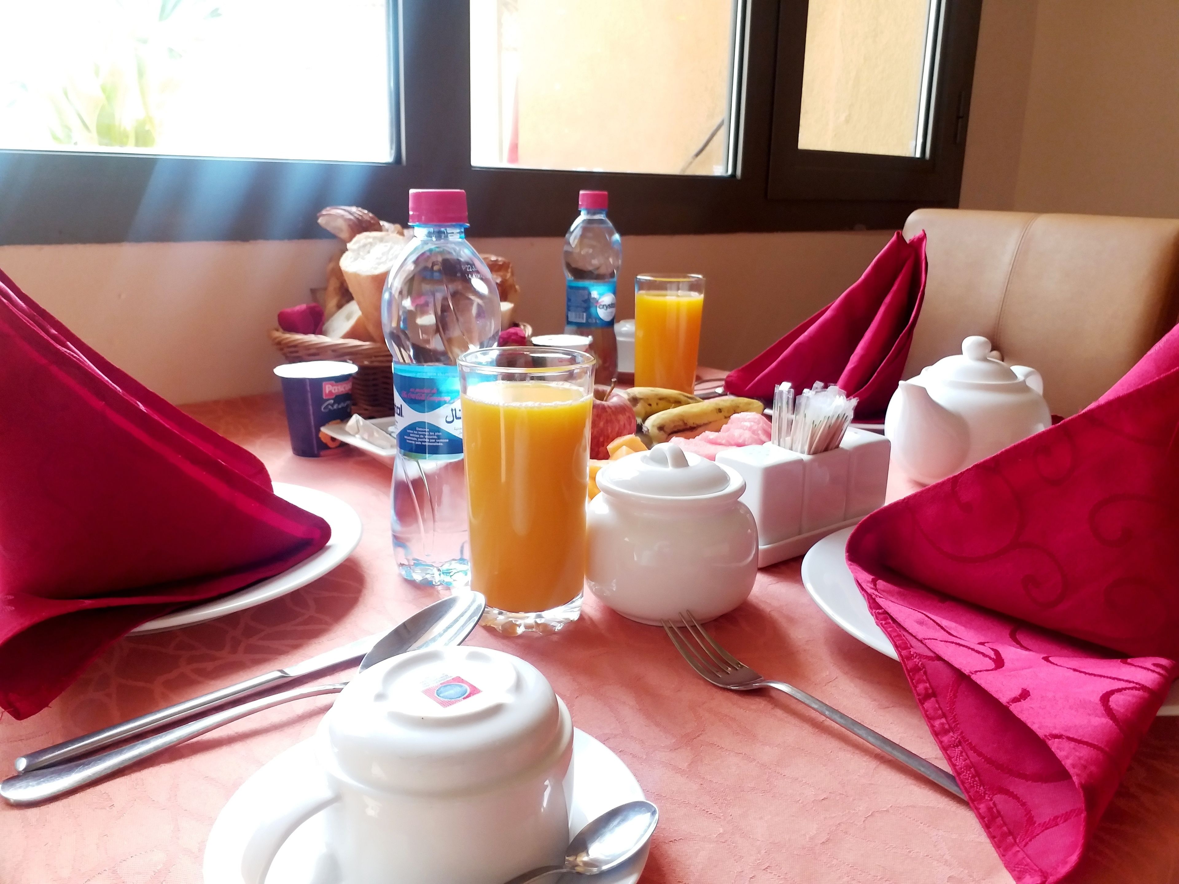 Una mesa con platos, cubiertos, tetera, jarra, botella y un vaso de zumo de naranja.