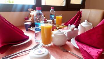 Una mesa con platos, cubiertos, tetera, jarra, botella y un vaso de zumo de naranja.