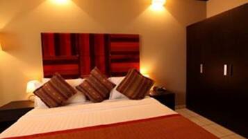 A hotel room with a bed, a nightstand, a wall-mounted TV, and a wardrobe.