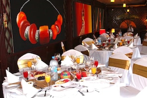 A restaurant setting with tables set for dining, featuring white tablecloths, gold sashes, and a variety of dishes and drinks.