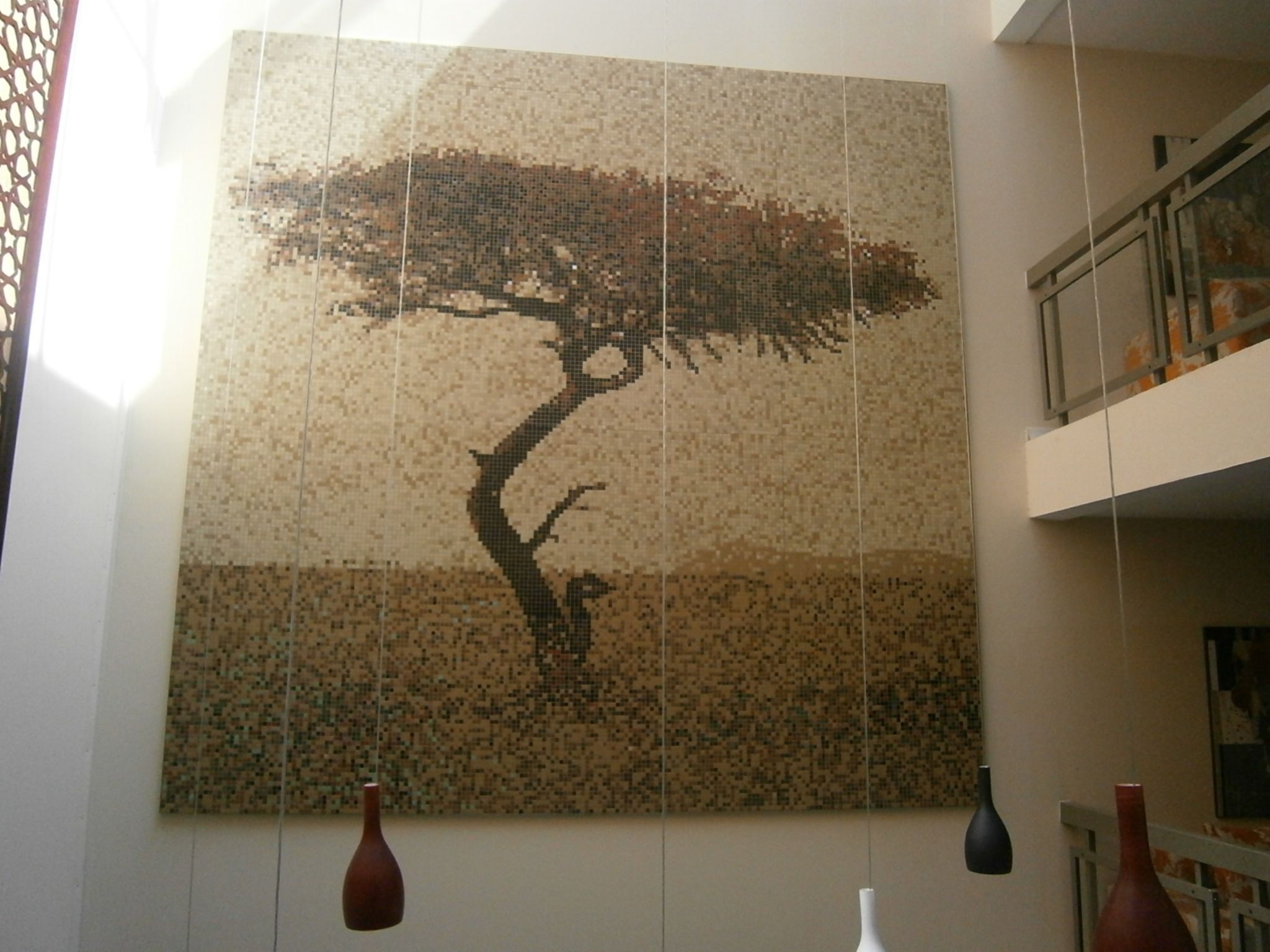 Un mur décoré d’une mosaïque représentant un arbre, des vases suspendus et un balcon agrémenté de balustrades.