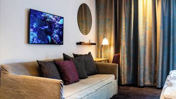 Habitación de hotel con sofá, televisor de pantalla plana, espejo, lámpara y cortinas.