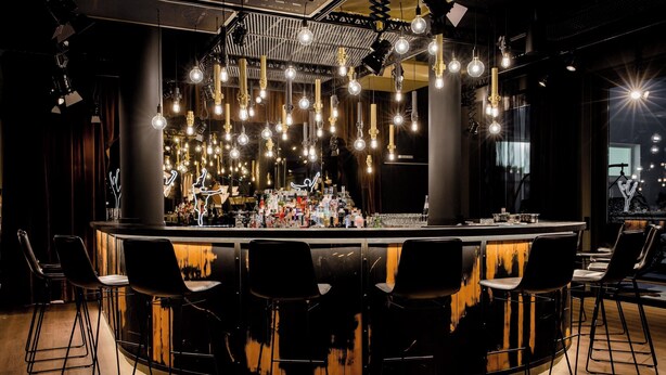 Een bar met een gebogen toonbank, meerdere hanglampen en barstoelen.