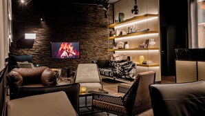 Een moderne woonkamer met een stenen muur, een flatscreen televisie, leren banken en een houten wandplank.