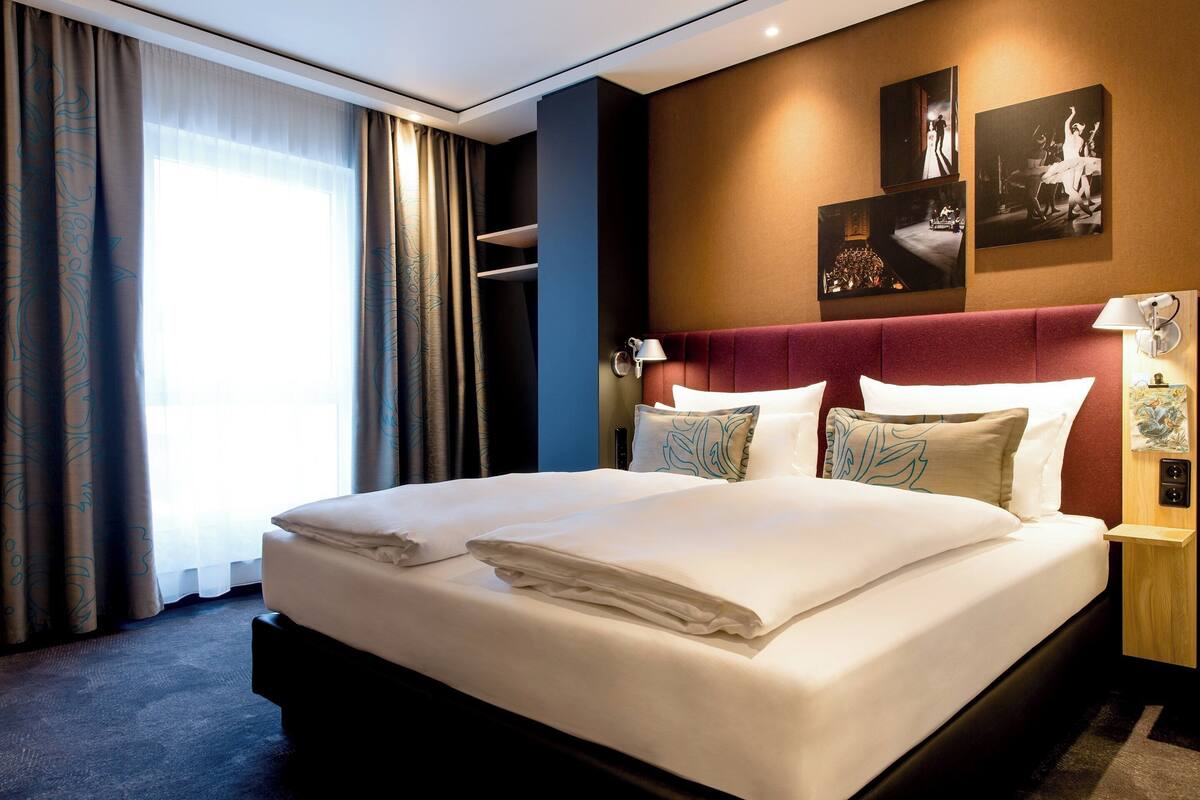Habitación de hotel con una cama grande, cabecero rojo y una pared con cuadros.