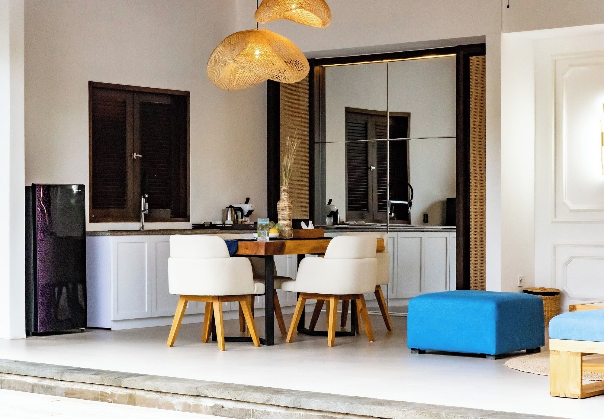 A modern kitchen with white cabinets, a dining table with four chairs, and a large mirror above the sink.