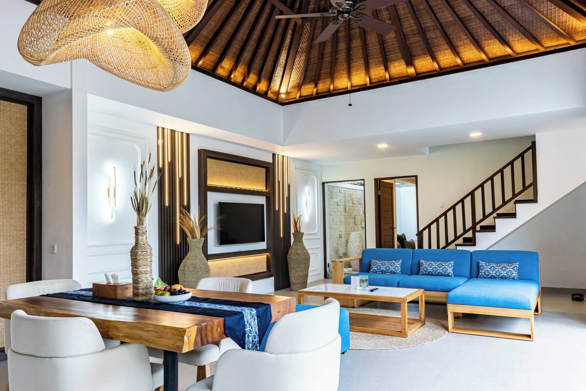 A modern living room with a wooden dining table, white sofas, and a blue sofa.