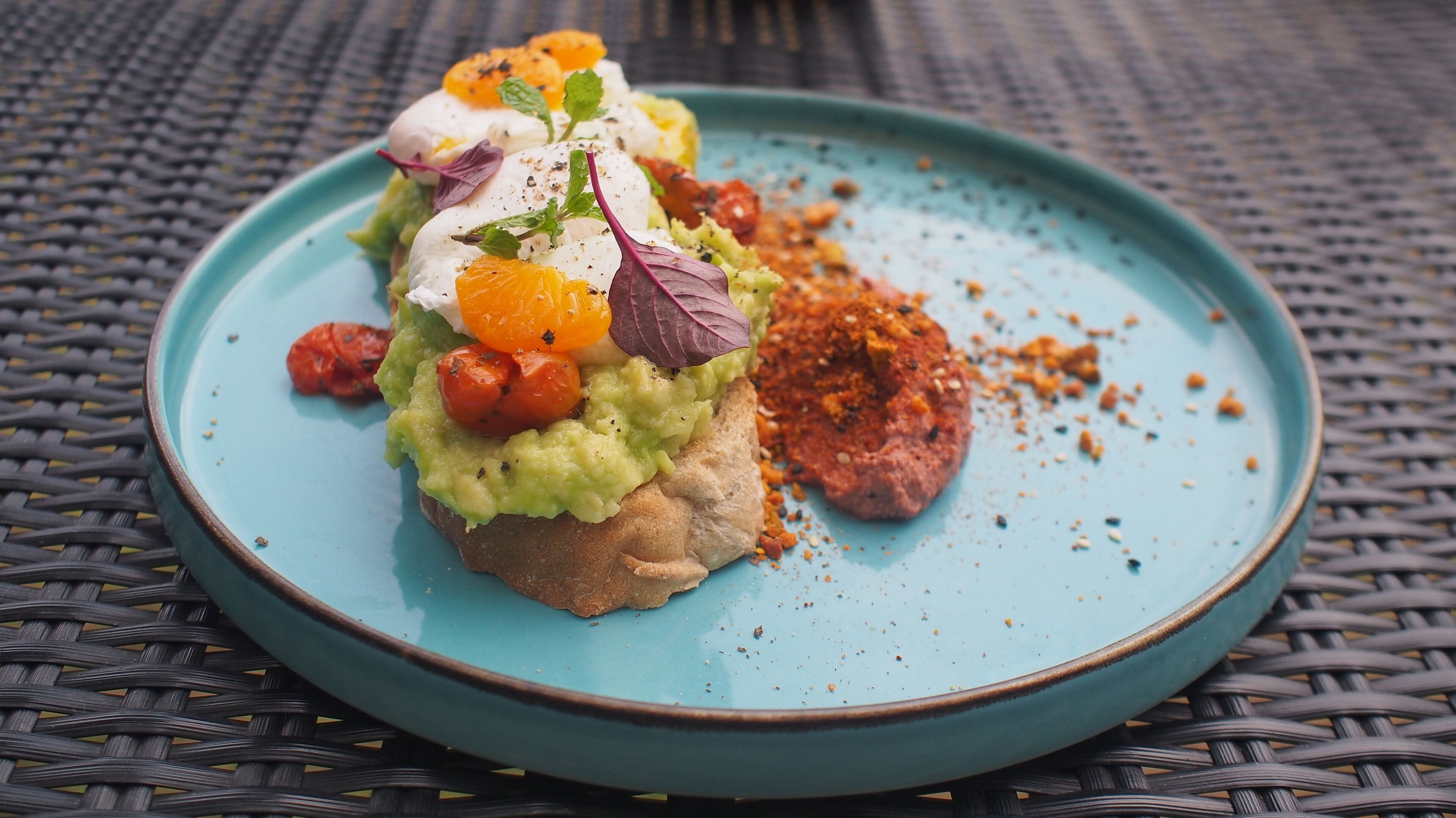 Un plato con un alimento cubierto de aguacate, tomates y un huevo escalfado, sobre un mantel tejido.