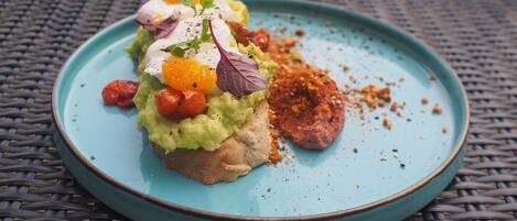 Un plato con un alimento cubierto de aguacate, tomates y un huevo escalfado, sobre un mantel tejido.