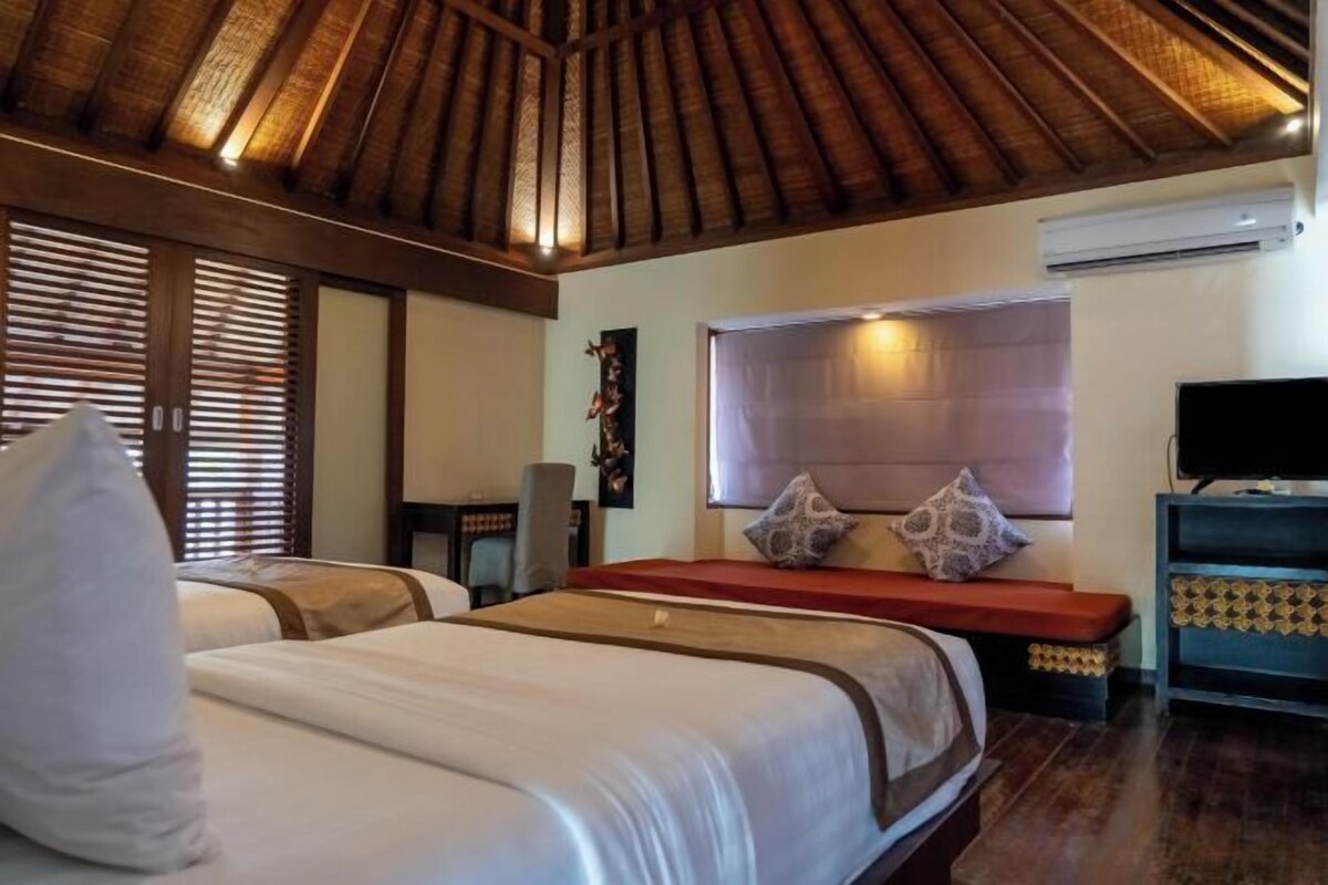 A hotel room with a wooden ceiling, a bed with white linens, a TV, and a window with blinds.