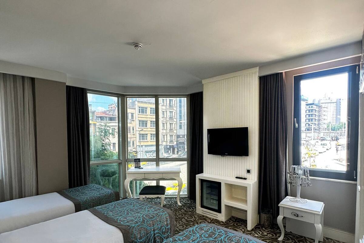 A hotel room with two beds, a TV, a small table, and a window with a city view.