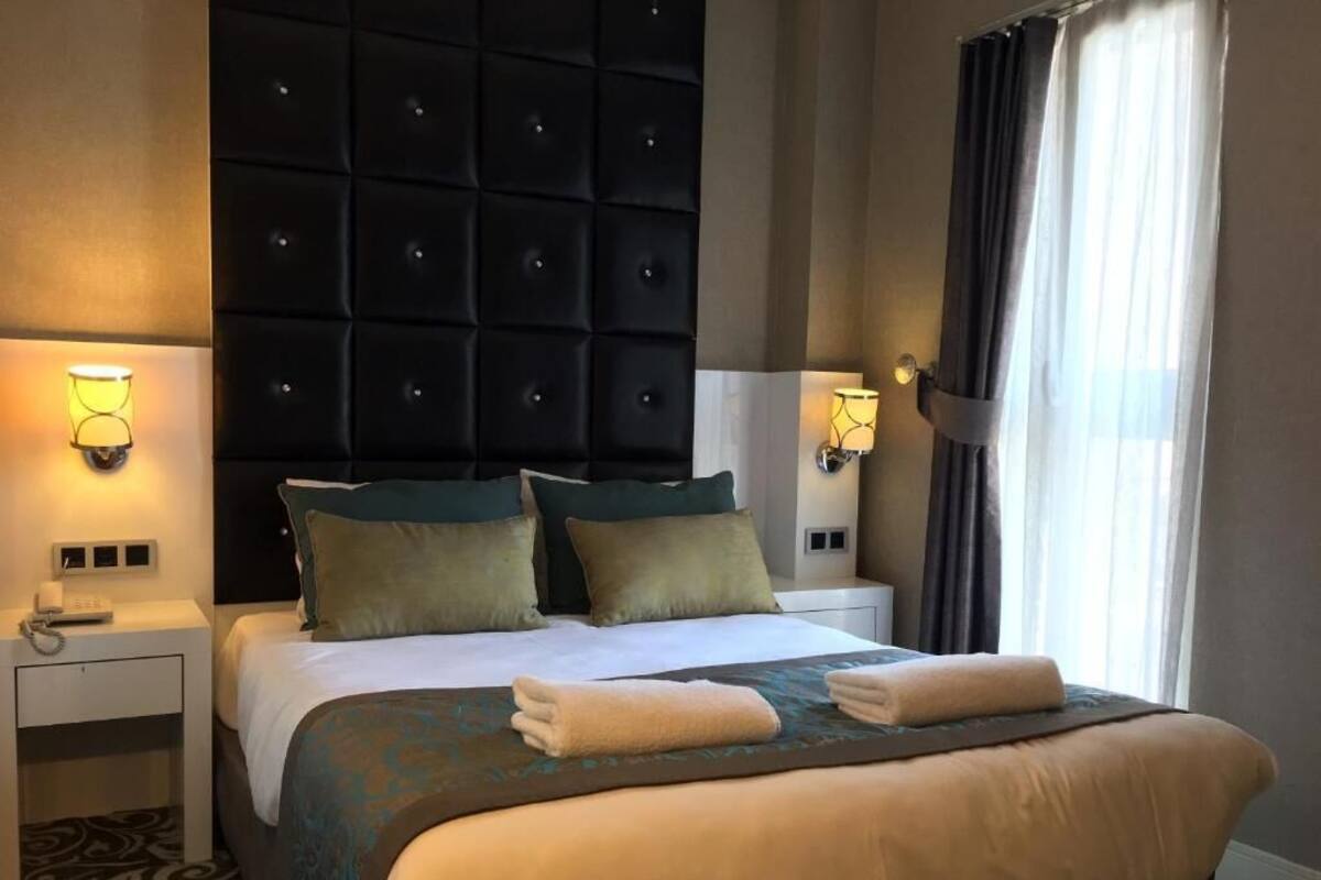 A hotel room with a large bed, two bedside tables, a tufted headboard, and a window with curtains.