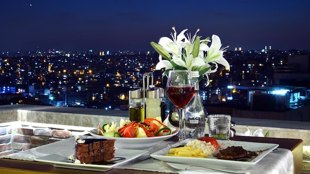 A table set with a dessert, salad, and plates of food, with a cityscape view in the background. - Taksim Line Hotel (Istanbul)