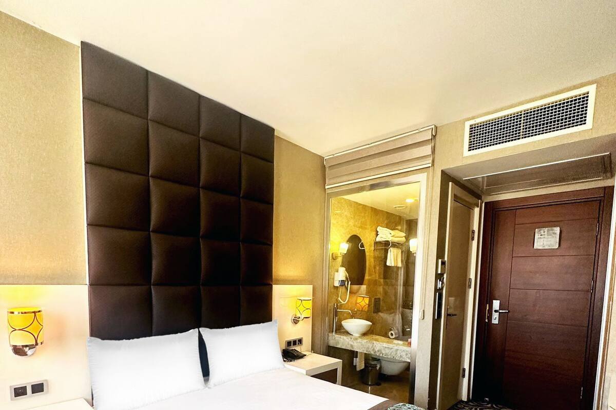 A hotel room with a large bed, a bathroom with a sink and mirror, and a door leading to another room.