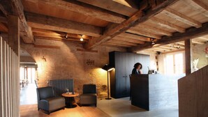 Un interior rústico con vigas de madera a la vista, una recepción y un área de estar con una lámpara.