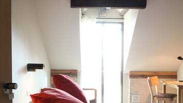 A bedroom with a bed, a red pillow, a wooden headboard, a desk, and a chair.