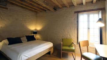 A bedroom with a wooden bed, a green chair, a wooden table, and a window with natural light.