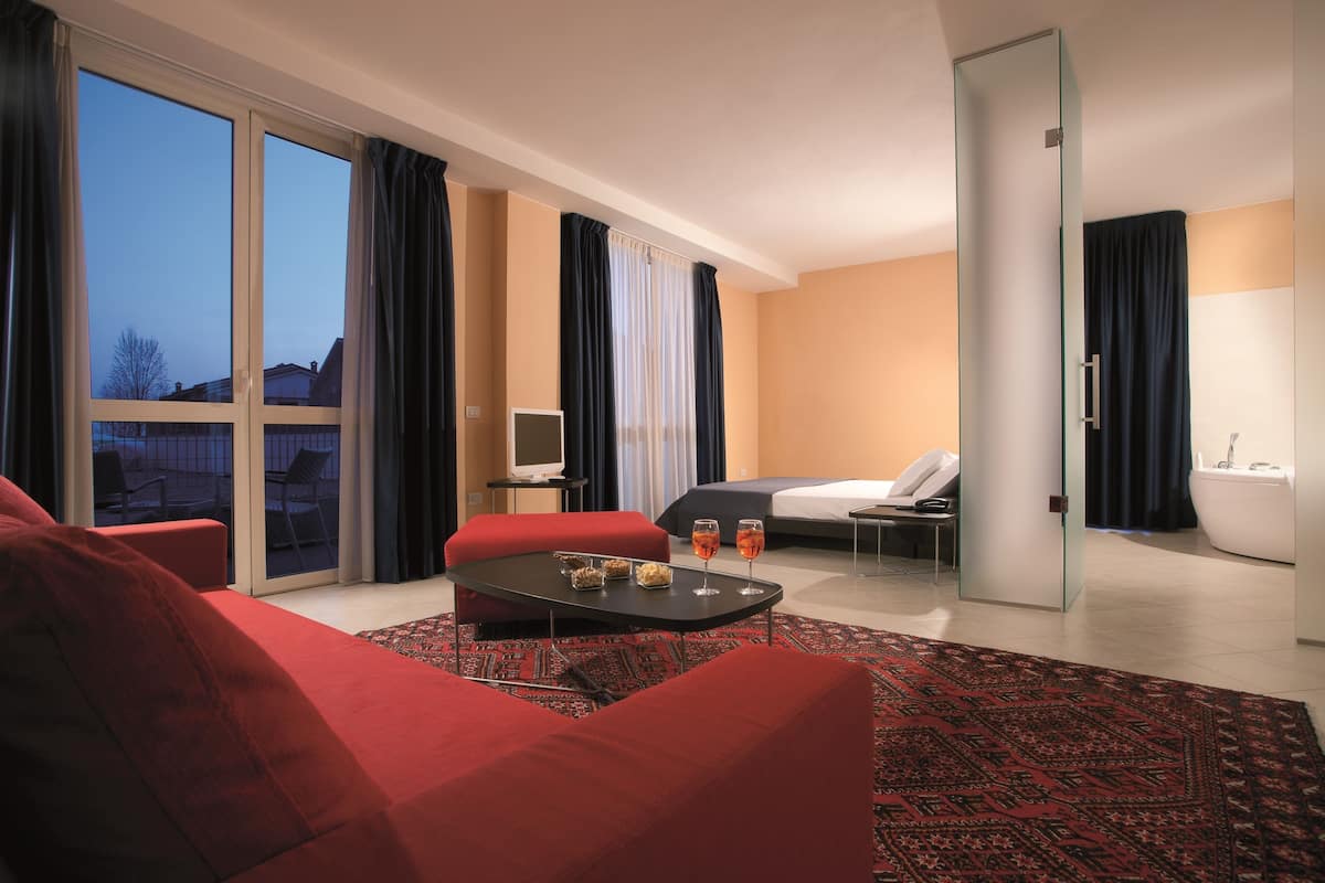 Een moderne hotelkamer met een groot raam, een rode bank, een klein tafeltje met glazen, een bed, een badkamer en een glazen deur.