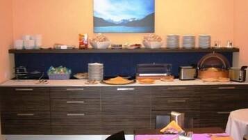 A kitchen with a dining area, featuring a buffet setup with various food items and a painting on the wall.