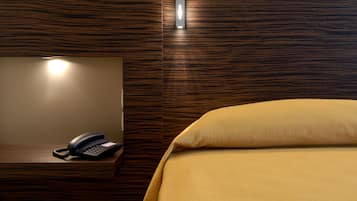 Ein Hotelzimmer mit hölzernem Kopfteil, einem Nachttischtelefon und einem ordentlich bezogenen Bett mit gelber Tagesdecke.