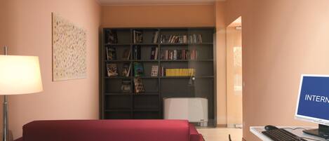 A room with a red sofa, a desk with a computer, a bookshelf, and a lamp.