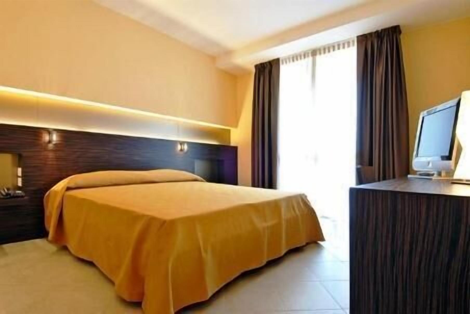 Une chambre d’hôtel avec un lit, un bureau équipé d’un ordinateur et une fenêtre avec des rideaux.