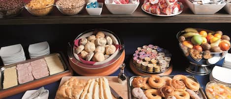 Un bufé con una variedad de alimentos, incluyendo panes, pasteles y frutas.