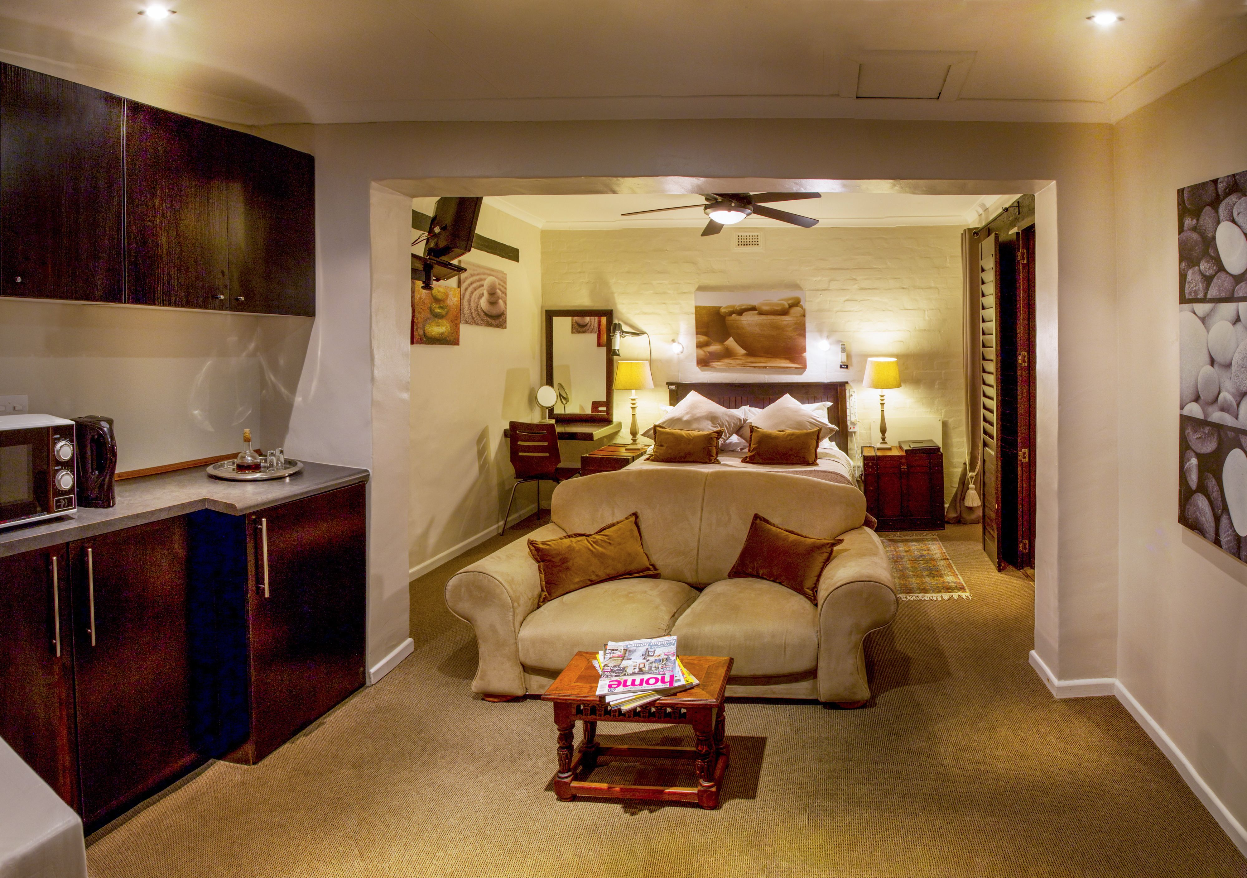 A hotel room with a bed, a sofa, a small table, a ceiling fan, a microwave, and a cabinet.