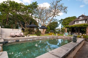 A swimming pool with a tiled border, surrounded by a garden with trees and outdoor furniture. - Forest Hall Guest House (Gqeberha (Port Elizabeth))