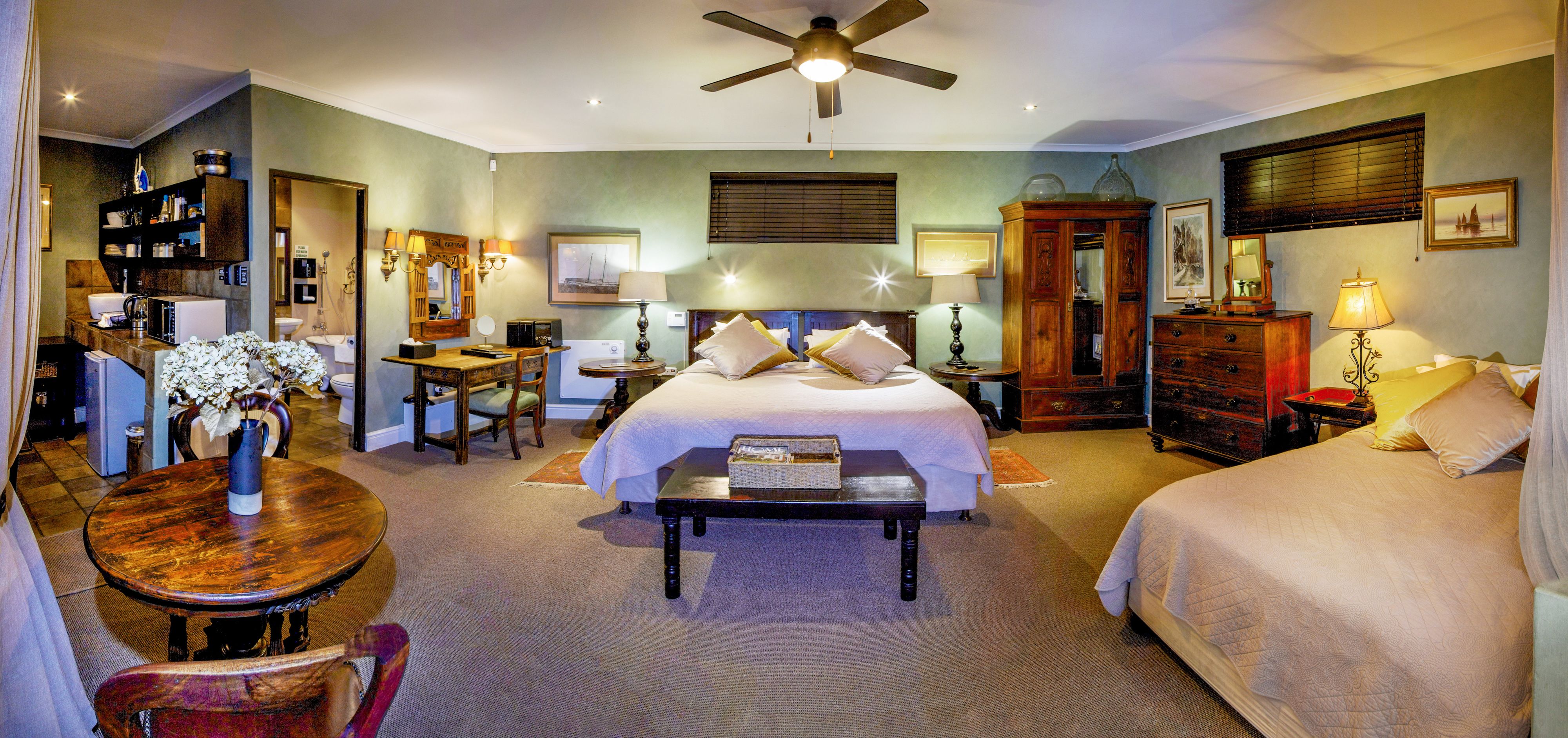 A hotel room with a bed, a desk, a chair, a table, and a ceiling fan.