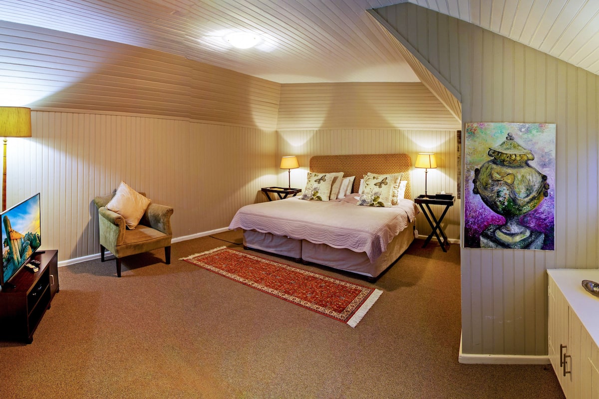 Een slaapkamer met een bed, nachtlampen, een televisie, een bureau met een computer en een schilderij.