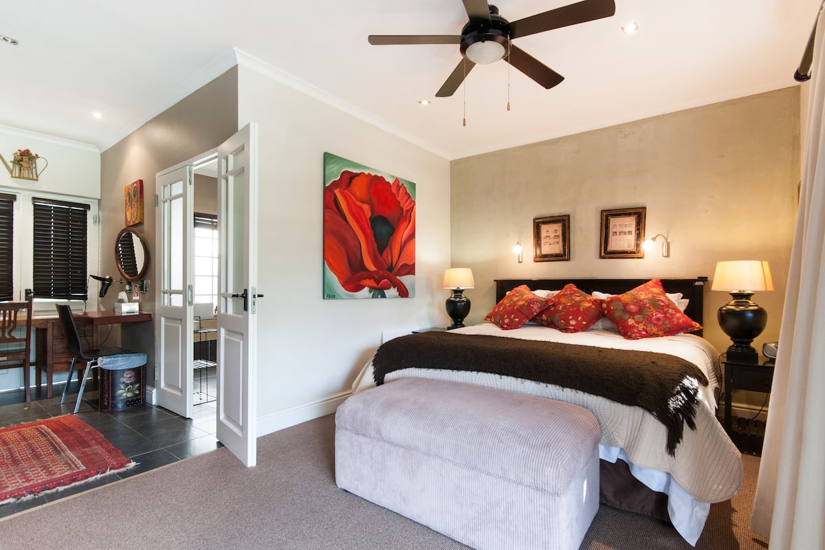 Een slaapkamer met een bed, nachtlampjes, een plafondventilator en een schilderij aan de muur.