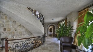 A grand staircase with ornate metal railings, a leather armchair, and a glass table in a spacious hallway with stone walls and large windows. - Goreme Inn Hotel +8 Adults Only (Nevsehir)