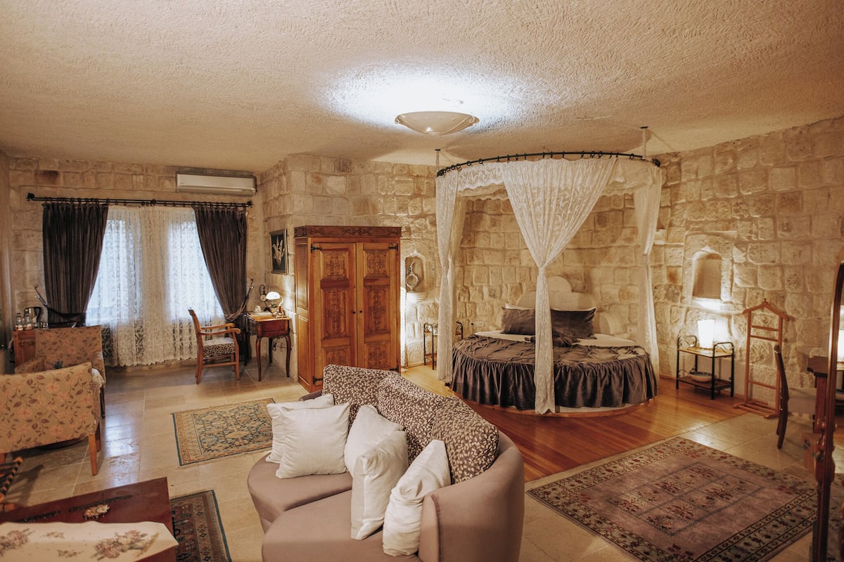 A room with a stone wall, a bed with a canopy, a sofa, a chair, and a small table.