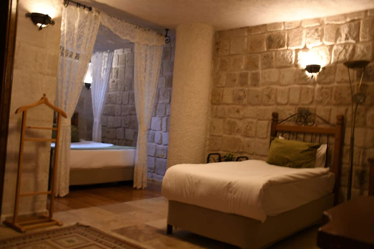 A bedroom with a stone wall, a bed with a wooden headboard, a hanging light fixture, and a bedside table.