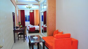 A hotel room with a red sofa, a small wooden table, a desk with a chair, and a bed with red curtains. - Al Qidra Hotel Aqaba (Aqaba)