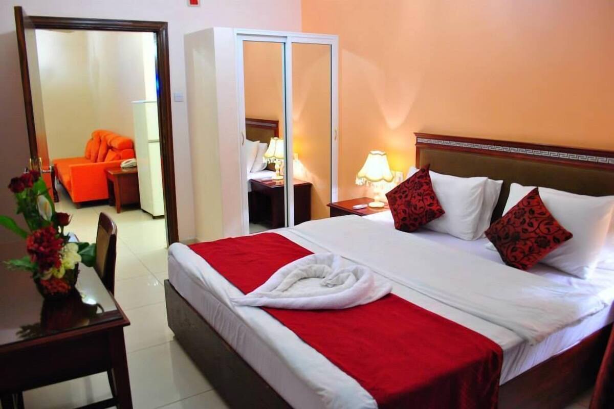 Een hotelkamer met een bed, een kledingkast, een bureau met stoel, en een spiegel.