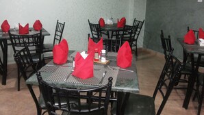 A dining area with tables set for four, each with a red napkin, black chairs, and a picture on the wall. - Al Qidra Hotel Aqaba (Aqaba)