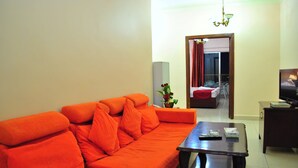 A living room with an orange sofa, a coffee table, a TV, and a potted plant. - Al Qidra Hotel Aqaba (Aqaba)