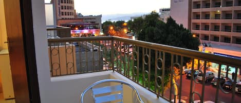 A balcony with a table and chairs, overlooking a busy street with cars and buildings, including a Days Inn sign.