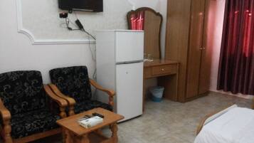 Una habitación con sofá, una mesita, un armario, un televisor montado en la pared y un refrigerador.