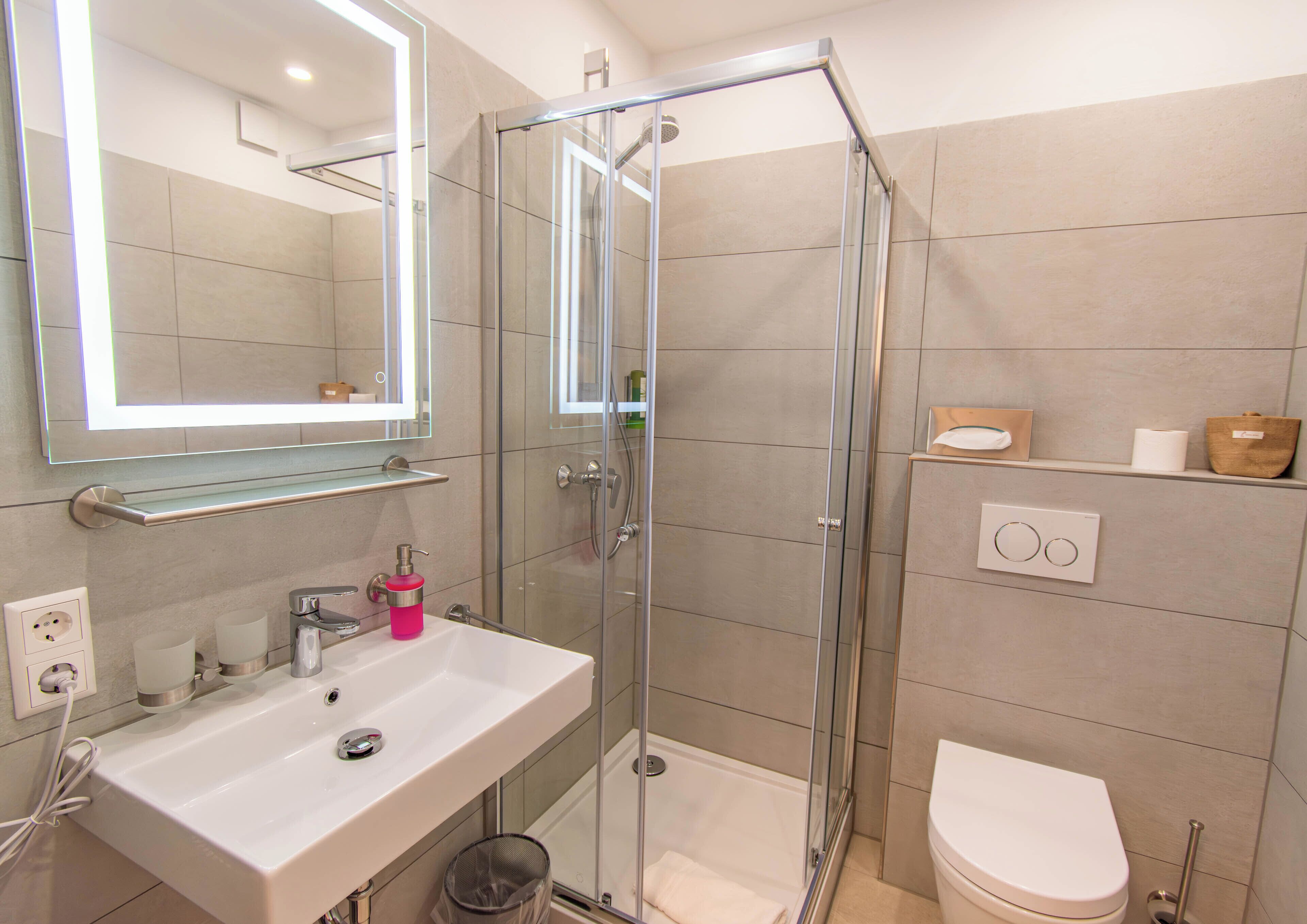 Un baño moderno con ducha de vidrio, un lavamanos blanco con espejo y un inodoro.