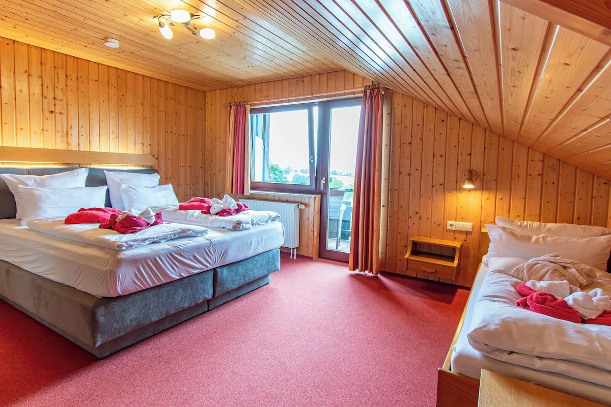 Quarto de cabana de madeira com duas camas, uma janela e teto de madeira.