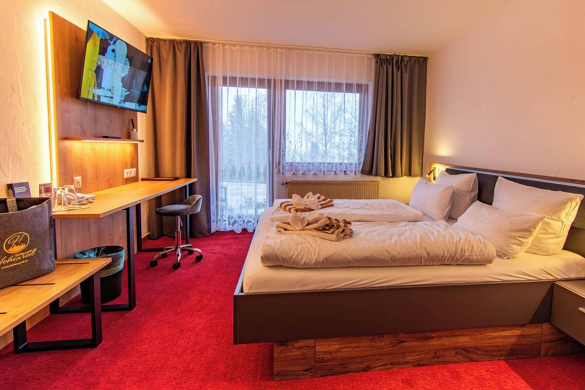 Quarto de hotel com cama, escrivaninha e televisão.
