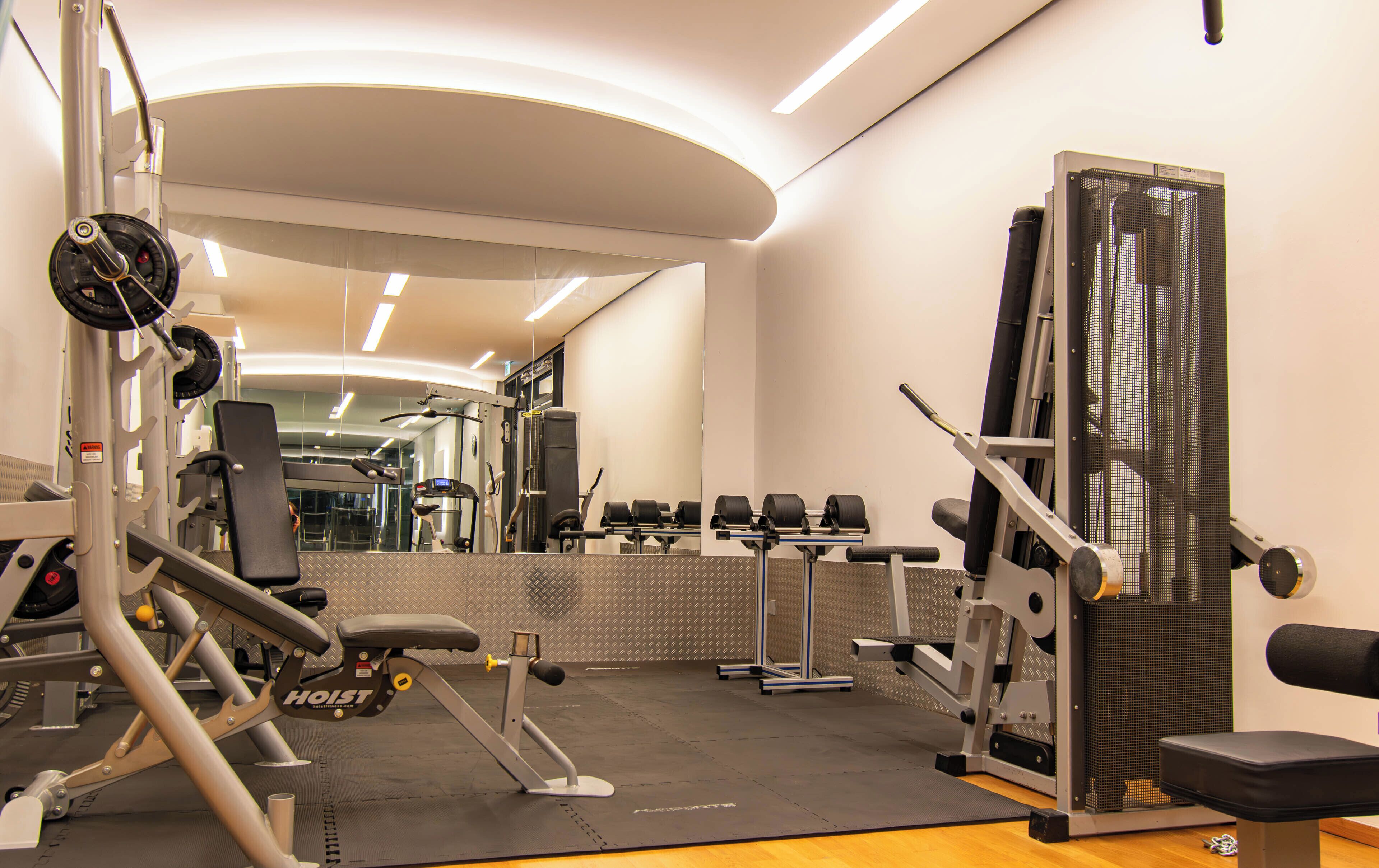 A gym with various exercise equipment, a mirrored wall, and a wooden floor.